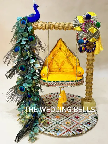 A divine Krishanji Jhula for Janmashtami. This design features a bright yellow quilted seat and a stunning arrangement of real peacock feathers, creating a majestic and traditional swing for Laddu Gopal.