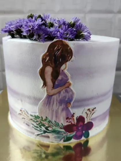 A beautiful baby shower cake for a mom-to-be. The design features a watercolor effect and is topped with fresh purple flowers.