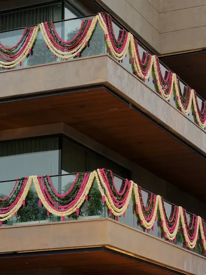 The exterior of the venue is adorned with beautiful garlands of pink, white, and green flowers, draping the balconies in festive color. This ensures the celebration's beauty is visible from the outside.