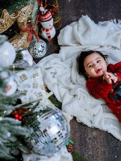 The pure joy of a baby's first Christmas. Lying on a soft blanket by the tree, this little one's happy smile perfectly captures the magic of the holiday season.