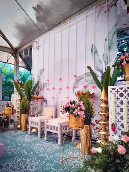 A modern take on traditional decor. This setup is perfect for a Shreemantham (baby shower) or housewarming, with a tropical leaf-print backdrop, gold accents, and pink florals.