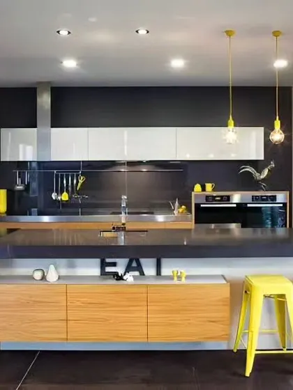 This modern kitchen features a large island with an "EAT" sign, making it a fun and social space. The yellow pendant lights and bar stools add a vibrant pop of color against the neutral cabinets.
