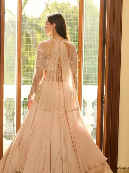 The back view of the off-white draped crop top lehenga, showcasing its unique design and embellished caped sleeves.