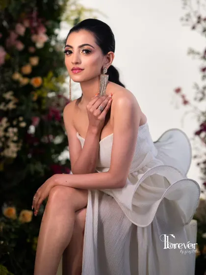 An editorial-style photoshoot look. The makeup is clean and elegant, with a focus on glowing skin and a defined eye, complementing the modern white dress.