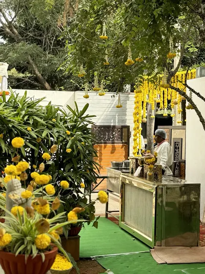 A wider view of the outdoor setup for the ceremony, showing the marigold-draped trees and a bar station, all blending seamlessly into the lush green environment.