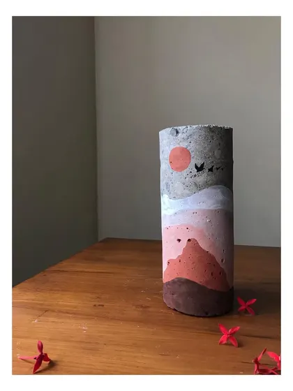 A close-up of the day-themed concrete sculpture. The earthy tones and simple depiction of a sun and birds create a warm, serene feeling. This hand-painted art piece is a perfect example of sustainable home decor.