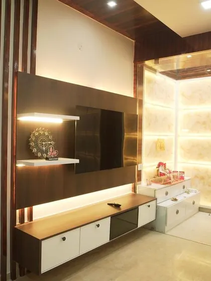 A combined TV and pooja unit, where the sacred space is enclosed in glass and illuminated with onyx marble panels. This design allows for spiritual devotion without compromising the living room's modern aesthetic.