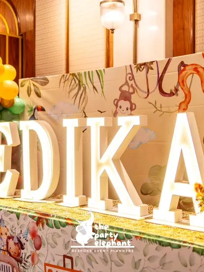 A close-up of the illuminated 'VEDIKA' letters, with the jungle-print backdrop and balloon clusters visible behind them.