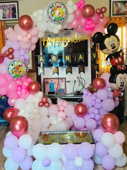 A cute Mickey and Minnie Mouse themed birthday setup with a pink, purple, and white balloon arch.