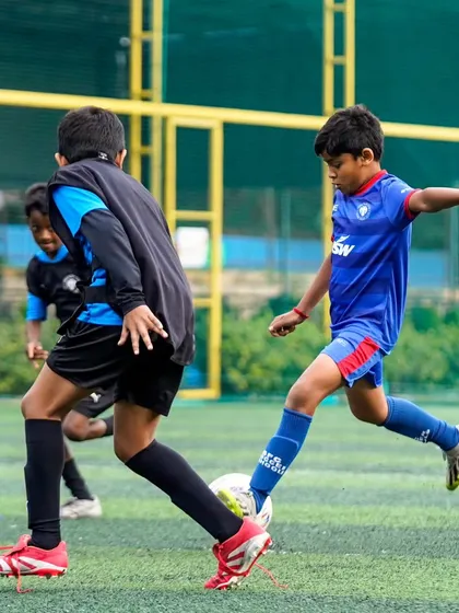 A player in our blue kit strikes the ball during a match. We teach proper shooting technique to help our players become clinical finishers.