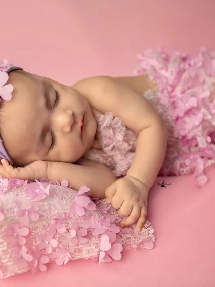 The perfect sleeping pose, with tiny hands tucked under a soft cheek. This image highlights the delicate features of a newborn in a beautiful, floral themed setup.