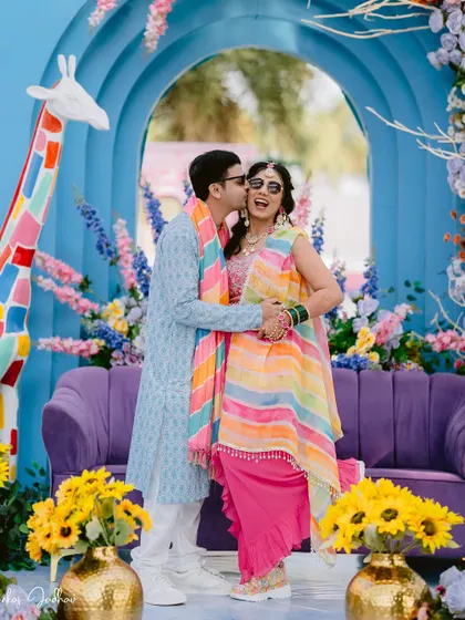 A sweet kiss on the cheek amidst the vibrant, playful decor of the Haldi function.