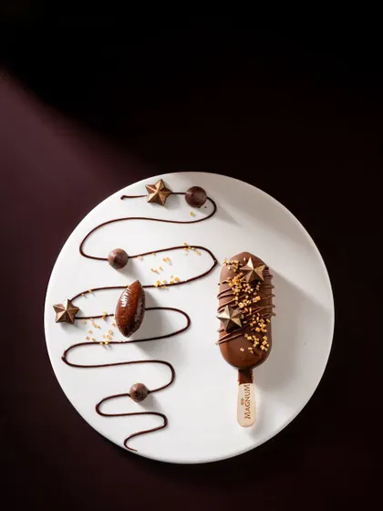 A minimalist and artistic presentation of a Magnum bar, using chocolate swirls and gold stars to create an elegant pattern on the plate.
