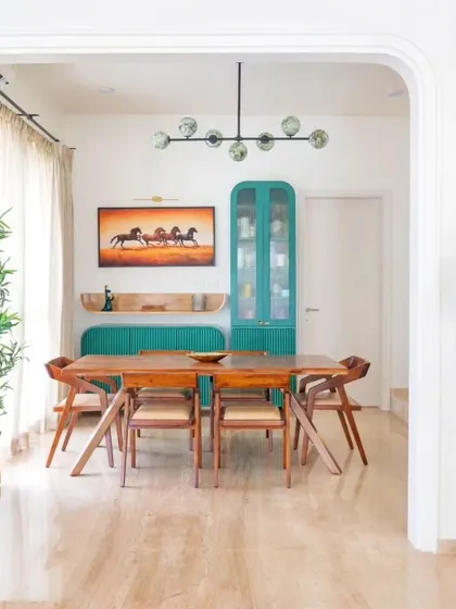 An inspiring living and dining area with bold teal cabinetry and a mid-century modern dining set, viewed through an elegant archway.