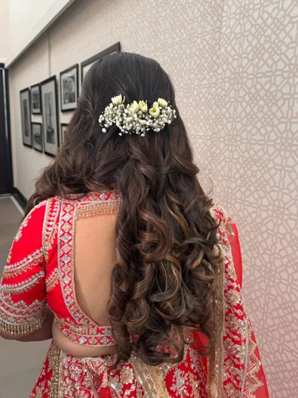 A beautiful half-updo with voluminous curls, accented with a barrette of fresh baby's breath. This is a romantic and modern choice for a wedding day.