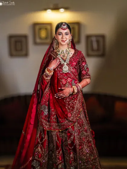 A full-length portrait of the bride in her magnificent red velvet lehenga. The rich fabric, intricate embroidery, and her graceful pose create a regal and breathtaking bridal image.