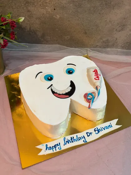 A fun, tooth shaped cake for a dentist's birthday, complete with a smiling face and a little tube of Colgate toothpaste.