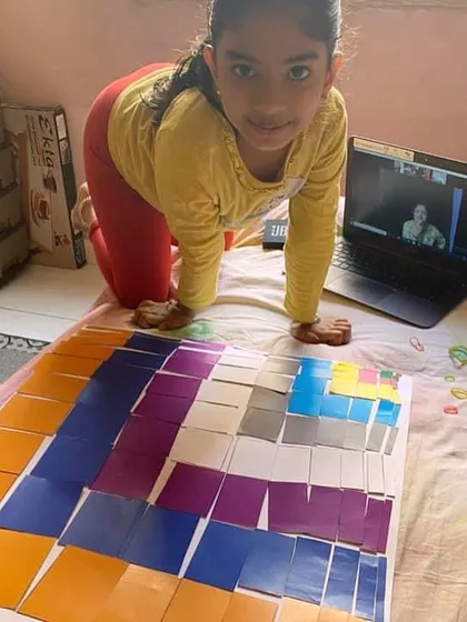A student completes the Decanomial Square at home. This advanced sensorial material provides a concrete basis for understanding squaring and the decimal system, bridging the gap between sensorial learning and abstract mathematics.