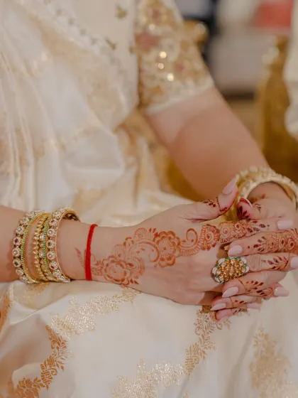 A close-up of the mother of the groom's hands, adorned with mehendi and beautiful jewellery, showcasing the detailed styling.
