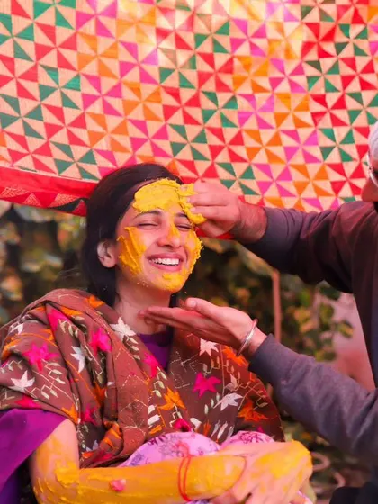 A playful moment during the Haldi ceremony. A family member gently applies turmeric to the bride's face, and her happy, scrunched-up smile is priceless.