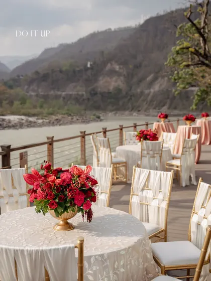 The guest seating area on the deck overlooking the Ganges. The tables were styled with crisp white linens and centerpieces of red flowers in brass urns, tying the entire look together.