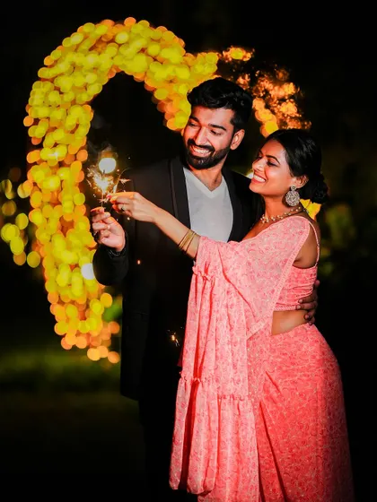 A magical night-time shot of a couple holding sparklers in front of a heart-shaped arch of lights, perfect for a festive pre-wedding theme.