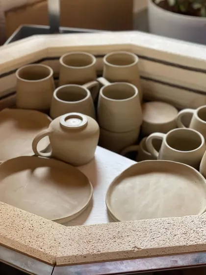 Mugs and plates loaded into the kiln for a bisque firing. This is a critical step before glazing, turning the fragile greenware into porous ceramic.