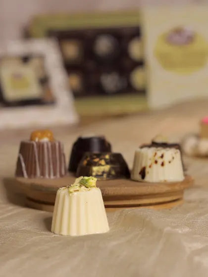 A closer look at our soft-center chocolates, each one a unique flavor experience. This assortment features our Pista Kunafa chocolate, a white chocolate shell filled with a nutty, textured center, alongside other decadent varieties.