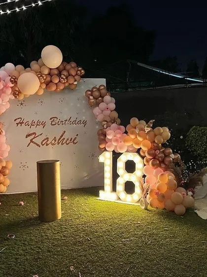 Here’s a chic 18th birthday I decorated on a terrace. I used marquee light-up numbers and a custom backdrop with the birthday person's name, framed by a stylish organic balloon arch in peach and rose gold tones for a sophisticated evening celebration.