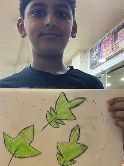 A student proudly displays his drawing of green leaves. Even simple subjects can become beautiful pieces of art.