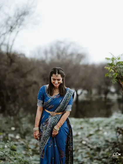 The bride looks down with a gentle smile, her blue saree and simple jewelry creating a look of understated elegance.