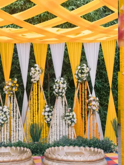 A beautiful Haldi ceremony backdrop featuring alternating drapes of yellow and white fabric, adorned with strings of marigolds and white flowers.