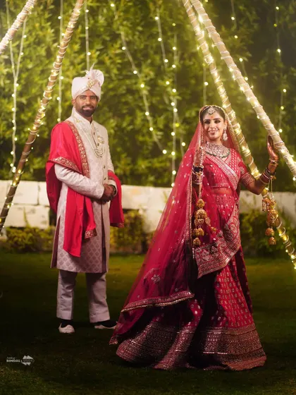 A full-length portrait of the couple in a garden setting, with fairy lights creating a magical ambiance. Their traditional attire looks stunning against the natural backdrop.