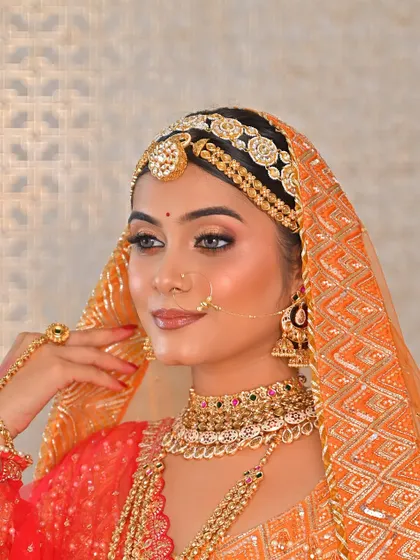 The epitome of bridal grace. The bride's look is completed with a beautiful orange bandhani dupatta over her head, framing her face and highlighting her flawless makeup.