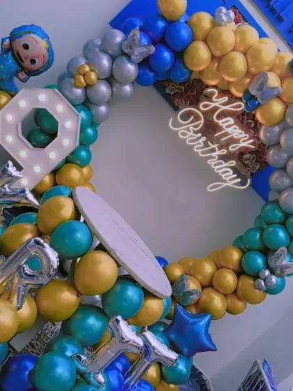 A Cocomelon-themed 9th birthday party. This full balloon ring uses blue, gold, and teal colors, with a Cocomelon character foil balloon and a light-up number '9'.