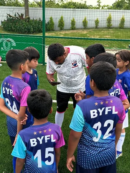 Coach Ashwin gathers his team for a pre-drill huddle. He uses a phone to visually explain the next exercise, ensuring the kids are ready and focused for the upcoming league preparation.