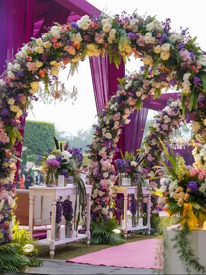 A beautiful double archway, completely covered in a mix of pastel and purple flowers, creates a fairytale entrance. The lighting from within makes the flowers glow.