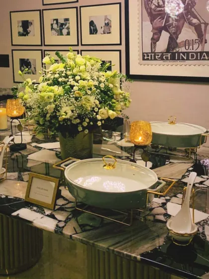 For intimate home gatherings, I create elegant buffet arrangements on marble top tables, complete with beautiful serving dishes, candles, and floral bouquets for a luxurious feel.