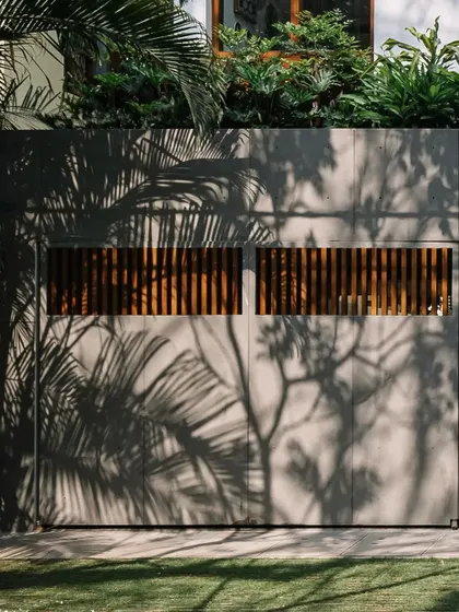 The play of shadows from tropical foliage on the home's concrete and wood facade creates a living, changing pattern throughout the day.