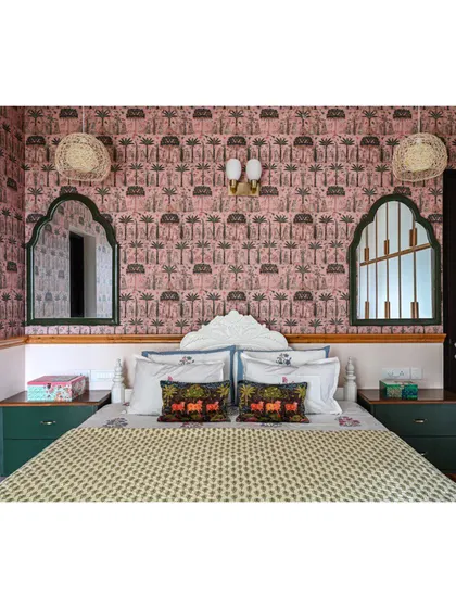 A full view of the guest bed, with its refinished white frame, Pichwai-print wallpaper, and arched mirrors.