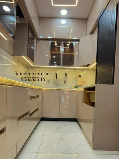 A full view of a U-shaped modular kitchen we delivered to a client. The design uses glossy beige cabinets with gold profile handles and extensive under cabinet and ceiling lighting for a bright, luxurious feel.