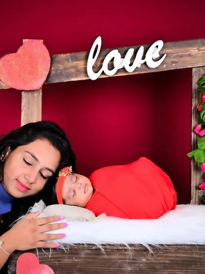 A mother gently resting her head next to her sleeping newborn in a "love booth" setup.