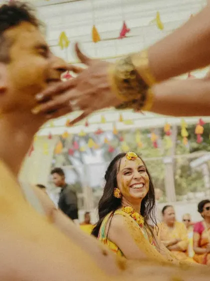 The bride watches with a huge smile as the groom gets playfully smeared with turmeric paste by family members.