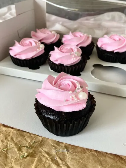 A close-up of a pretty pink strawberry-filled cupcake. The simple rosette and pearl sprinkles add an elegant touch.