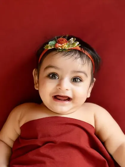 A close-up of a happy baby girl wrapped in red fabric, smiling for the camera.
