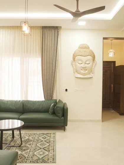 A serene living room in a villa, featuring deep green sofas and a large Buddha head sculpture as a calming focal point. The space is designed for relaxation and peace.