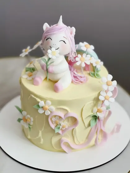 This sweet unicorn cake features a hand-sculpted unicorn topper smelling a daisy. Our figurine classes focus on creating expressive characters with charming details.