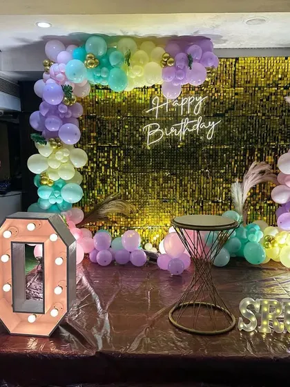 A fun and colorful 10th birthday decoration with a gold shimmer wall, pastel balloon arch, and large marquee numbers.
