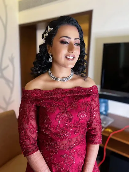 This bride's reception style is all about elegance. Her off-the-shoulder red gown is paired with beautiful curls and a radiant makeup look that highlights her smile.
