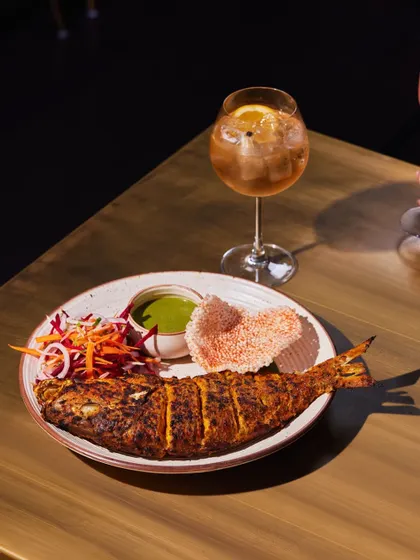 Another angle of our whole tandoori red snapper, perfectly cooked and ready to be shared, paired with a refreshing cocktail.